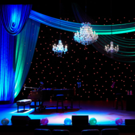 chandelier hanging over a brightly lit multi-colored stage. fabric is draped framing the stage