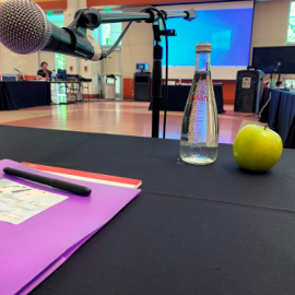 image of a professional desk space. A microphone, clipboard and presentation screen are visible. 